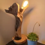 Lampe à poser en bois flotté dont la forme évoque un poing. l'ampoule est allumée