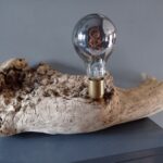 Lampe unique sur socle en bois flotté avec une ampoule Edison sur un meuble moderne.