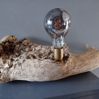 Lampe unique sur socle en bois flotté avec une ampoule Edison sur un meuble moderne.