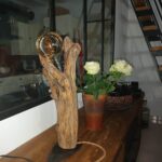Bois flotté en hauteur qui donne l'impression de représenter un trophée réalisé par Kalos Wood. Une ampoule est positionnée en haut de la sculture naturelle.