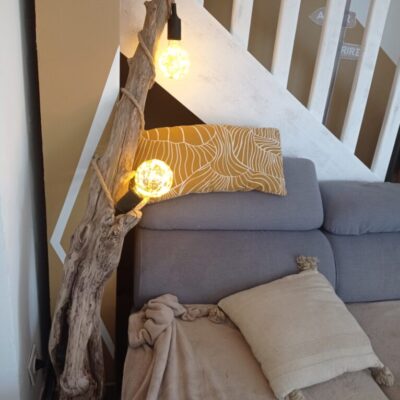 Lampe en bois flotté qui s'élance vers le plafond. Pièce d'art mise en situation dans un salon.